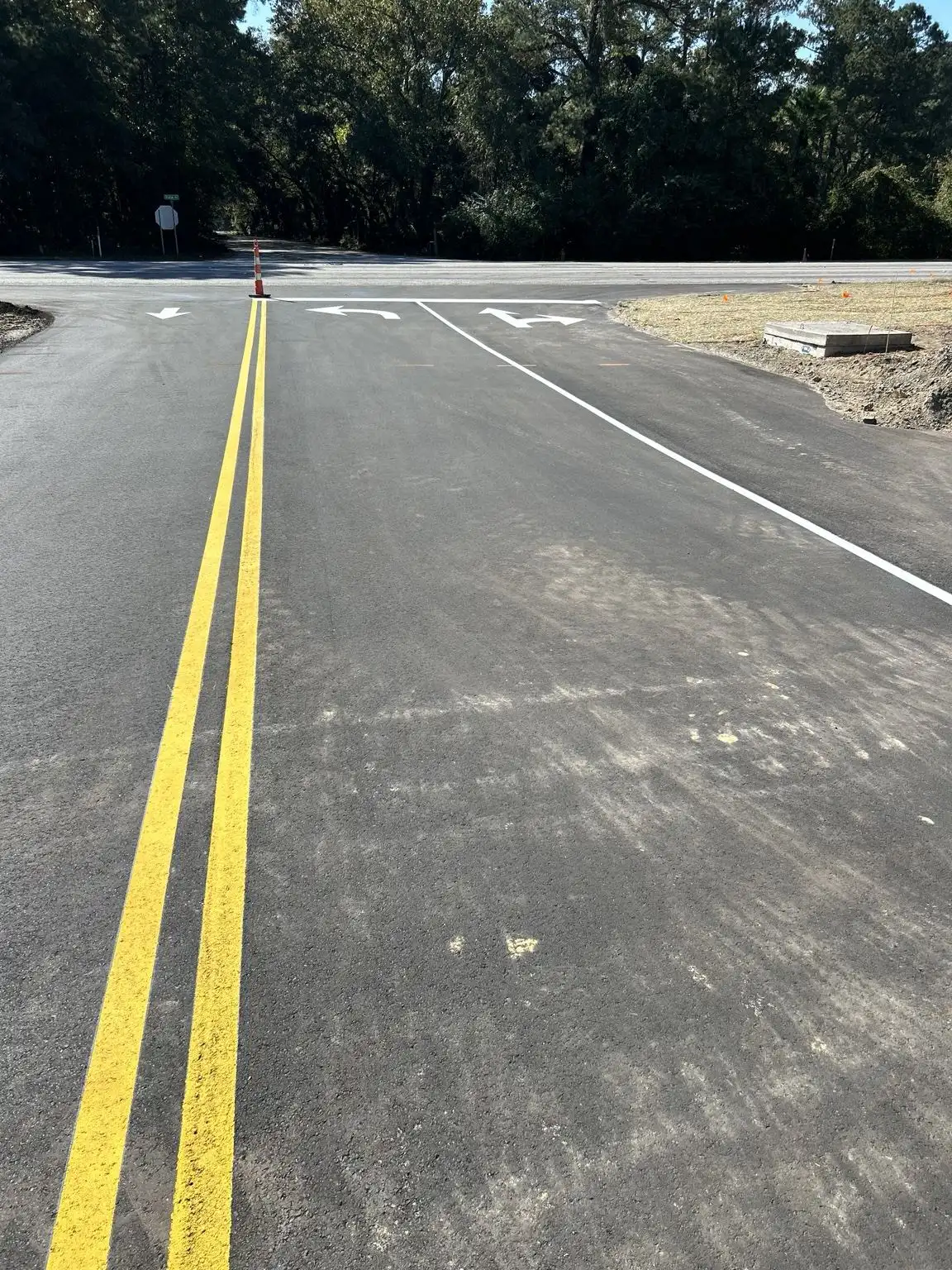 New asphalt roadway with double yellow centerline, white lane lines and directional arrows